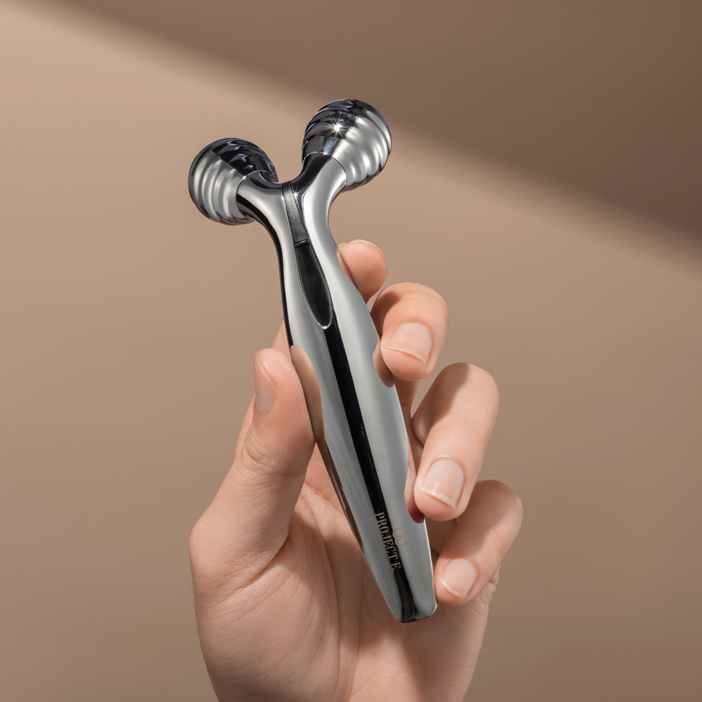 Hand holding the chrome-finished Vora Mild Microcurrent Facial Roller by Project E Beauty.